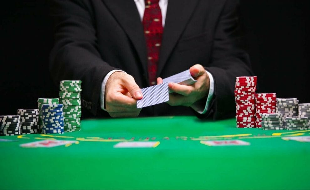 a man in a suit dealing a card at a green poker table between stacks of poker chips 