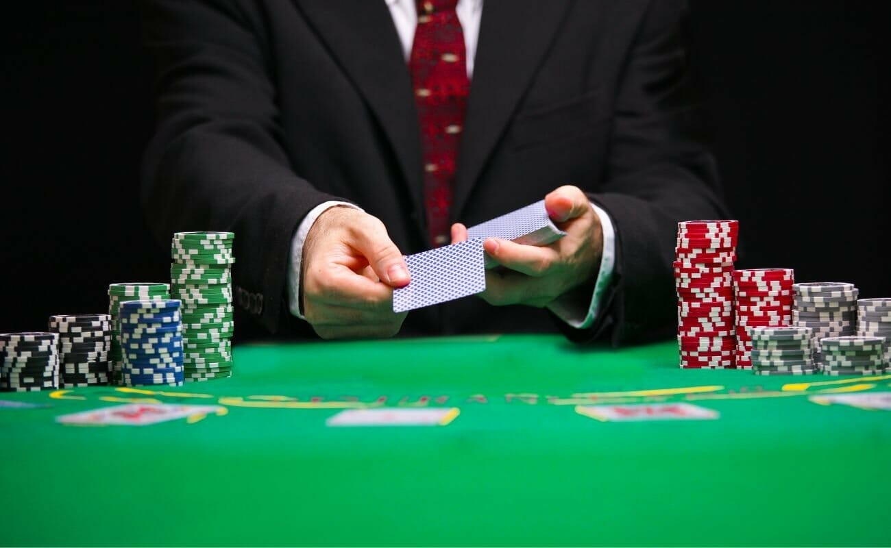 a man in a suit dealing a card at a green poker table between stacks of poker chips