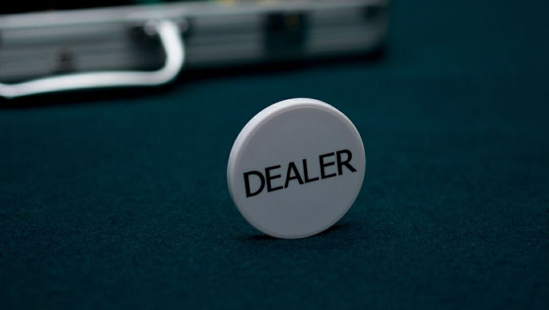 a dealer chip standing upright on a green felt poker surface with a briefcase of poker chips in the background