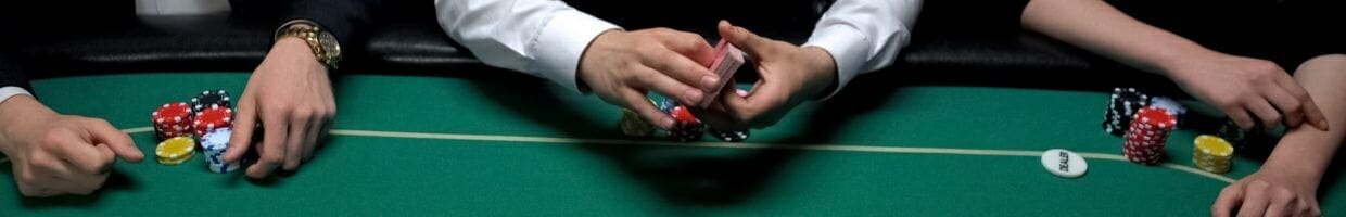 Hero Image, close up of three peoples arms at a poker table with poker chips in front of them, the croupier in the middle holds a deck of cards