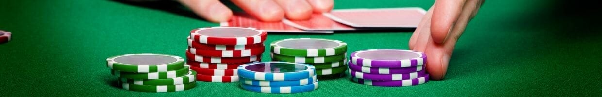 Poker chips stacked in front of three face down playing cards at a poker table with a man’s hands touching the poker chips and cards