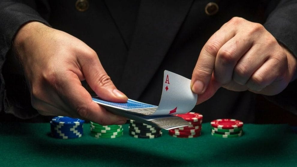 Body image, man sitting at a poker table with stacks of poker chips on it, he holds a deck of playing cards and is pulling an ace of diamonds out of the deck 