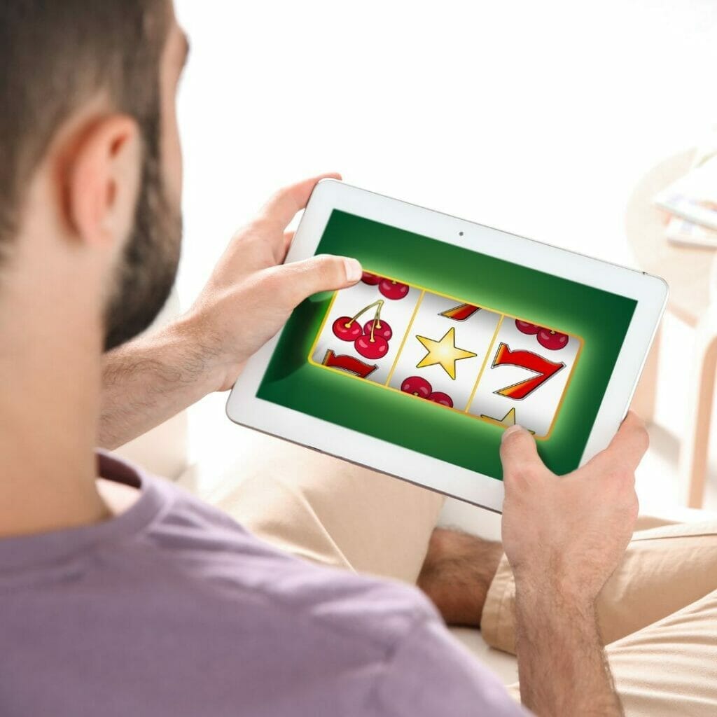 Header image, man playing online slots on a digital tablet device while sitting