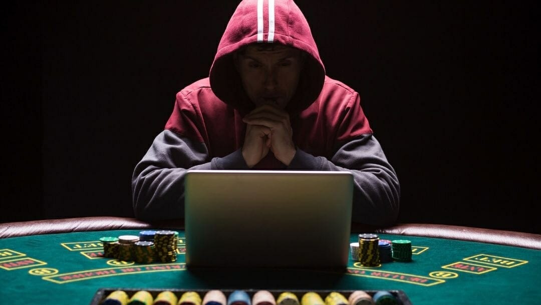 Body image, a man wearing a hoodie sitting at a poker table with a laptop in front of his and his hands clasped together at his chin 