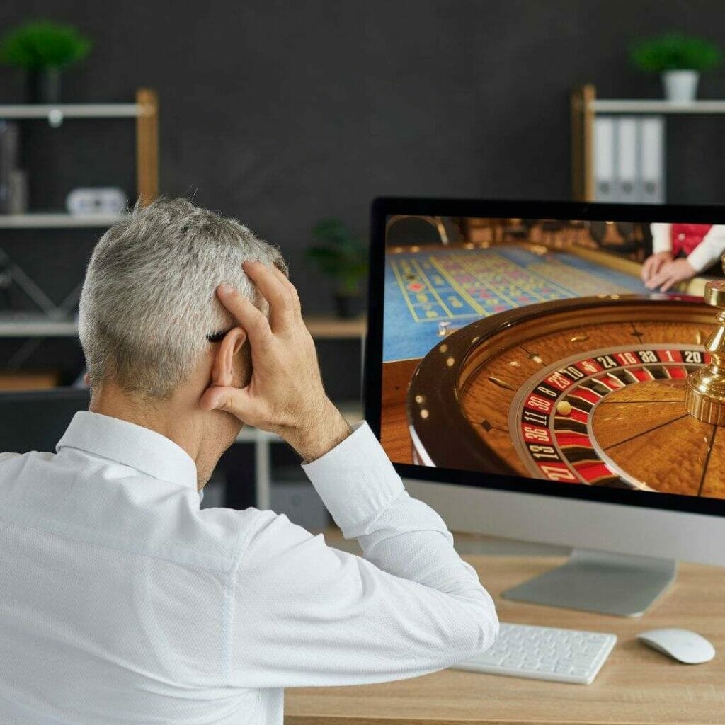 back shot of a man playing online roulette on a computer, his hands are on his head in anticipation.