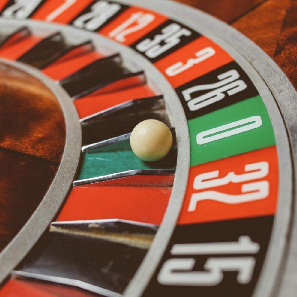 close up of a vintage wooden roulette wheel with the little white roulette ball on the number zero