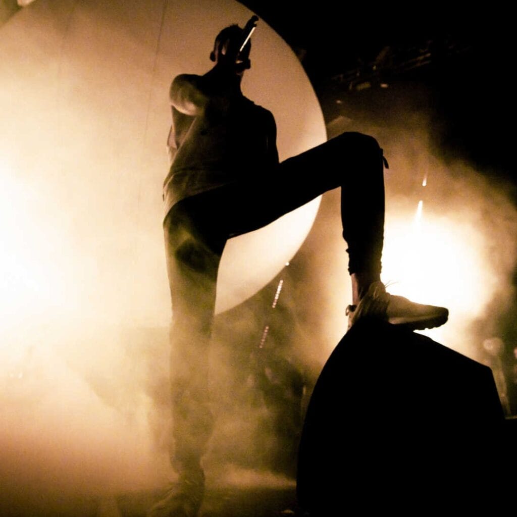 Silhouette of a singer on stage with their foot up on the speaker.
