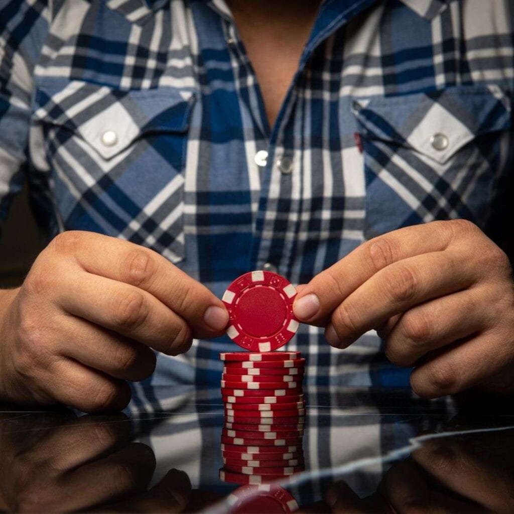 a man is sitting at a table holding the top poker chip from a stack of red poker chips