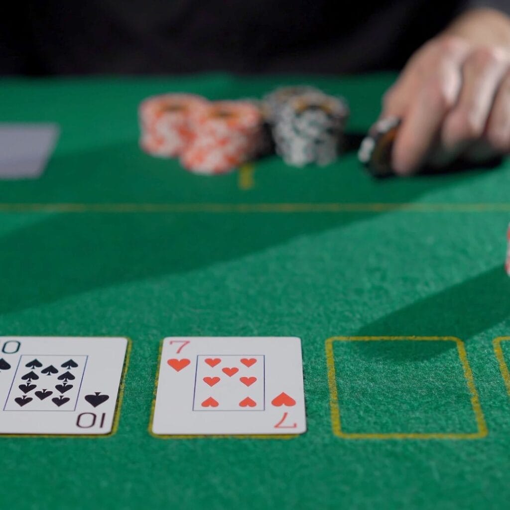 playing cards on a green felt poker table with a player holding a poker chip in the background with stacks of poker chips