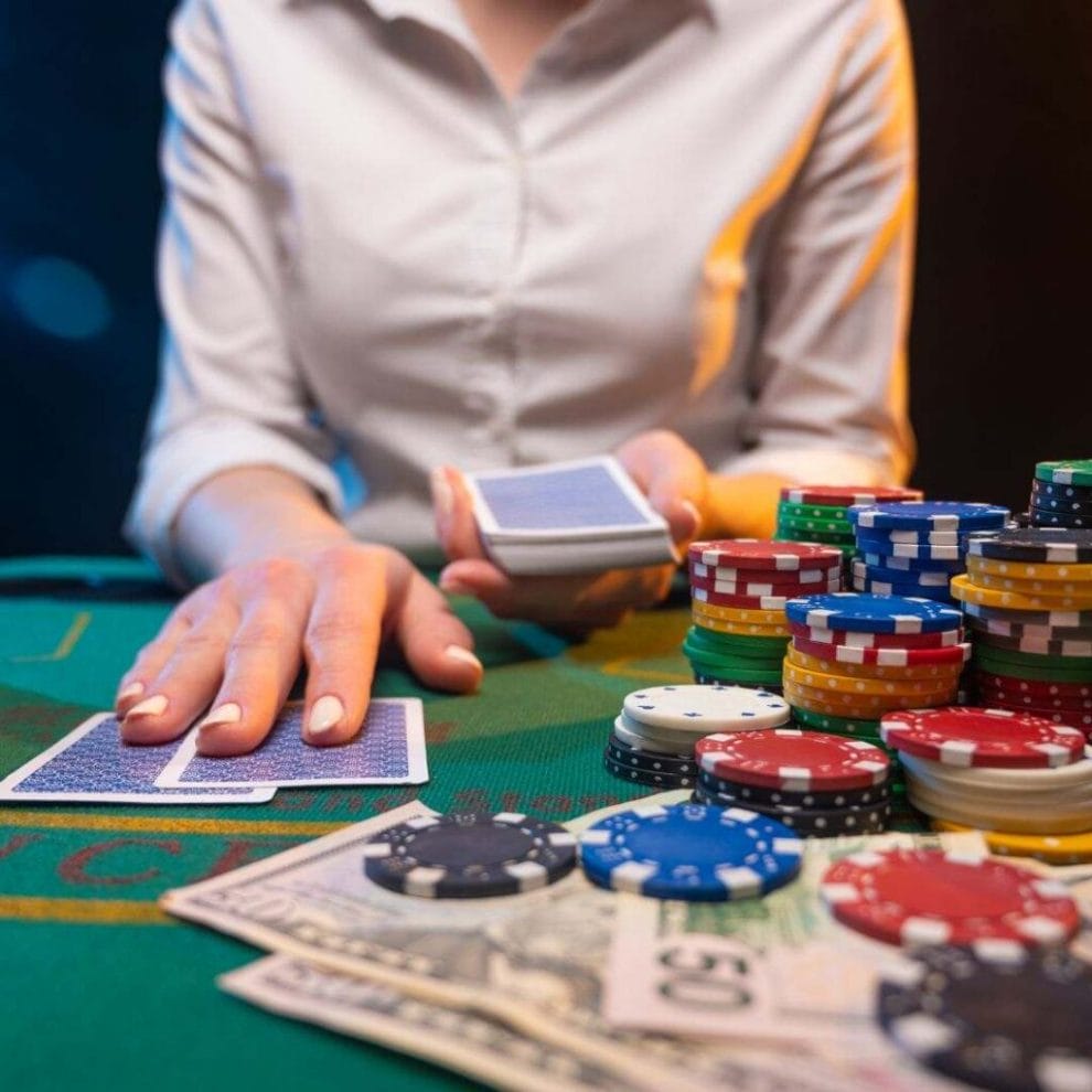 a woman dealer dealing two playing cards on a green blackjack table that has stacks of poker chips and money notes on it