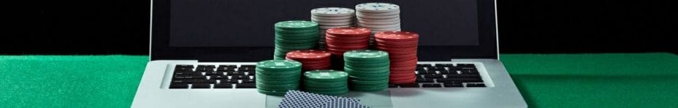 stacks of poker chips and a pair of playing cards on a laptop keyboard on a green felt poker surface