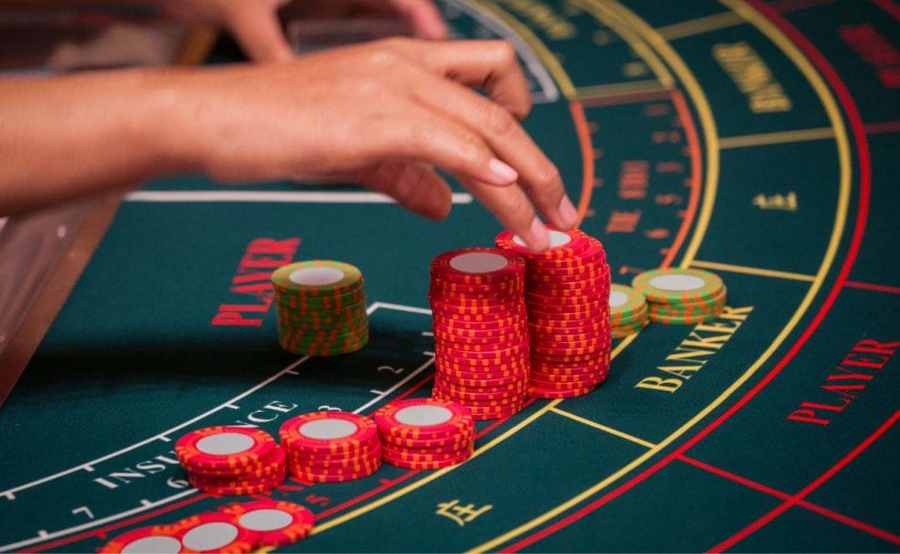 a dealer’s hand organizing the red and green baccarat chips on a baccarat gaming table in a casino