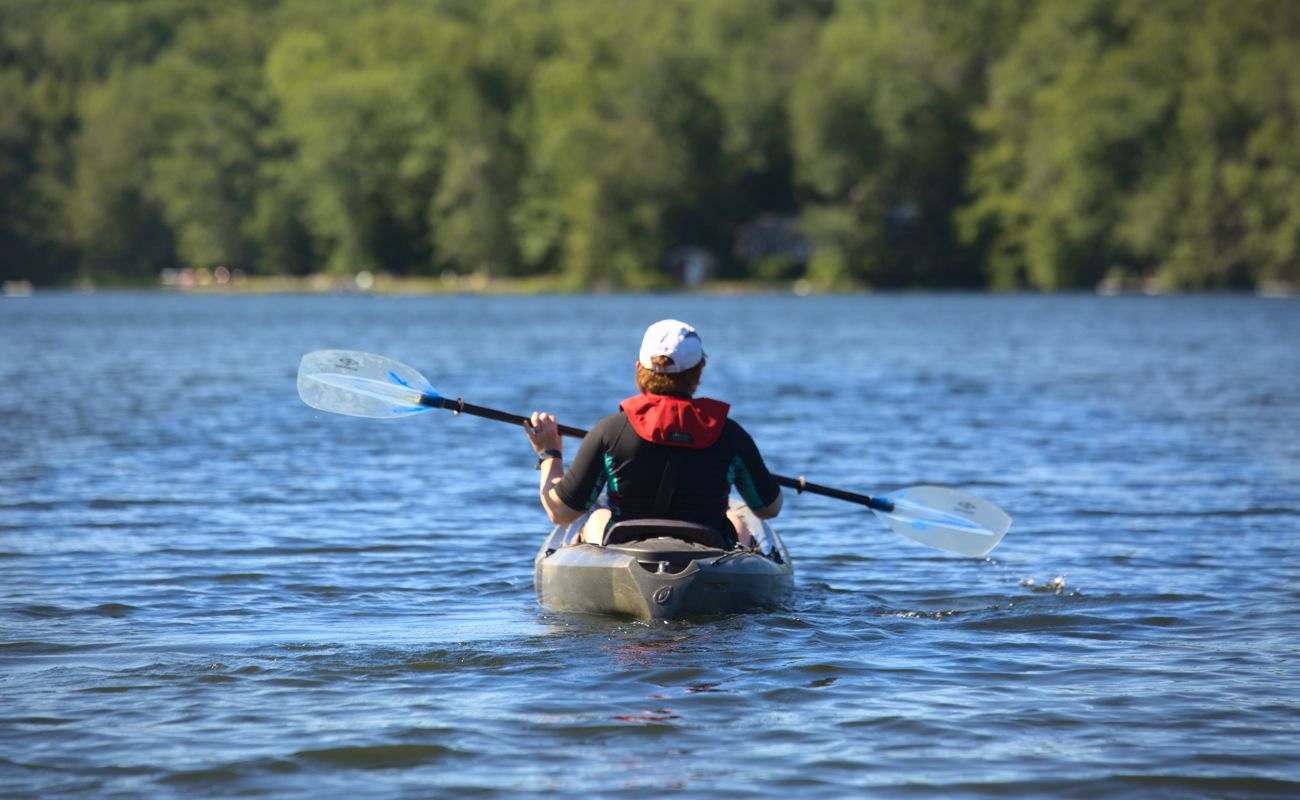  A person kayaking on a lake with a forest visible on the shore.