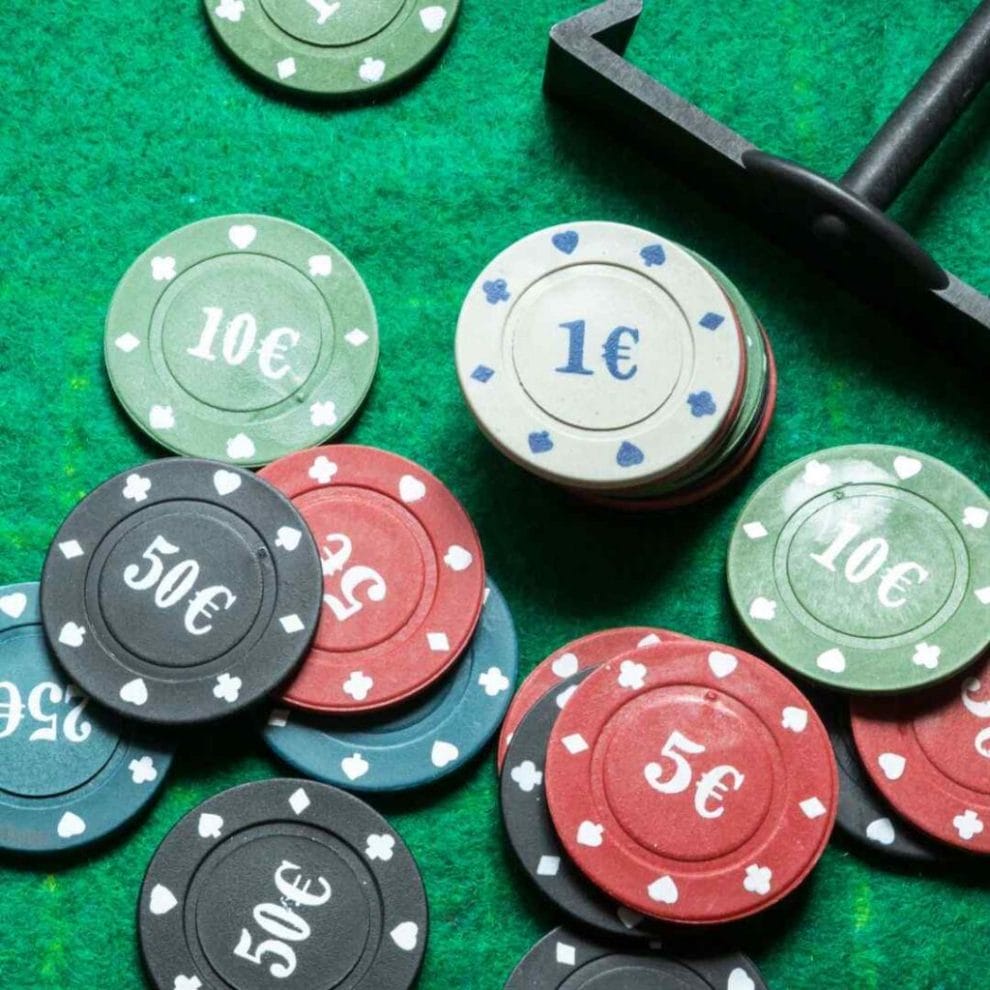 multi-colored poker chips and a poker chip rake on a green felt poker surface