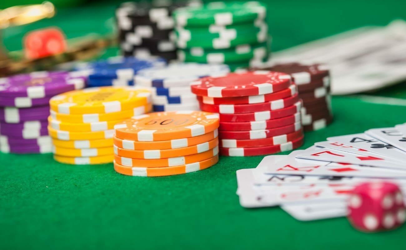 multi-colored stacks of poker chips on a green felt poker table next to a hand of playing cards and a red dice