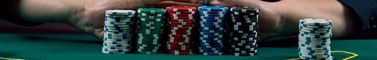 six stacks of poker chips on a green felt poker table with a person’s arms in the background