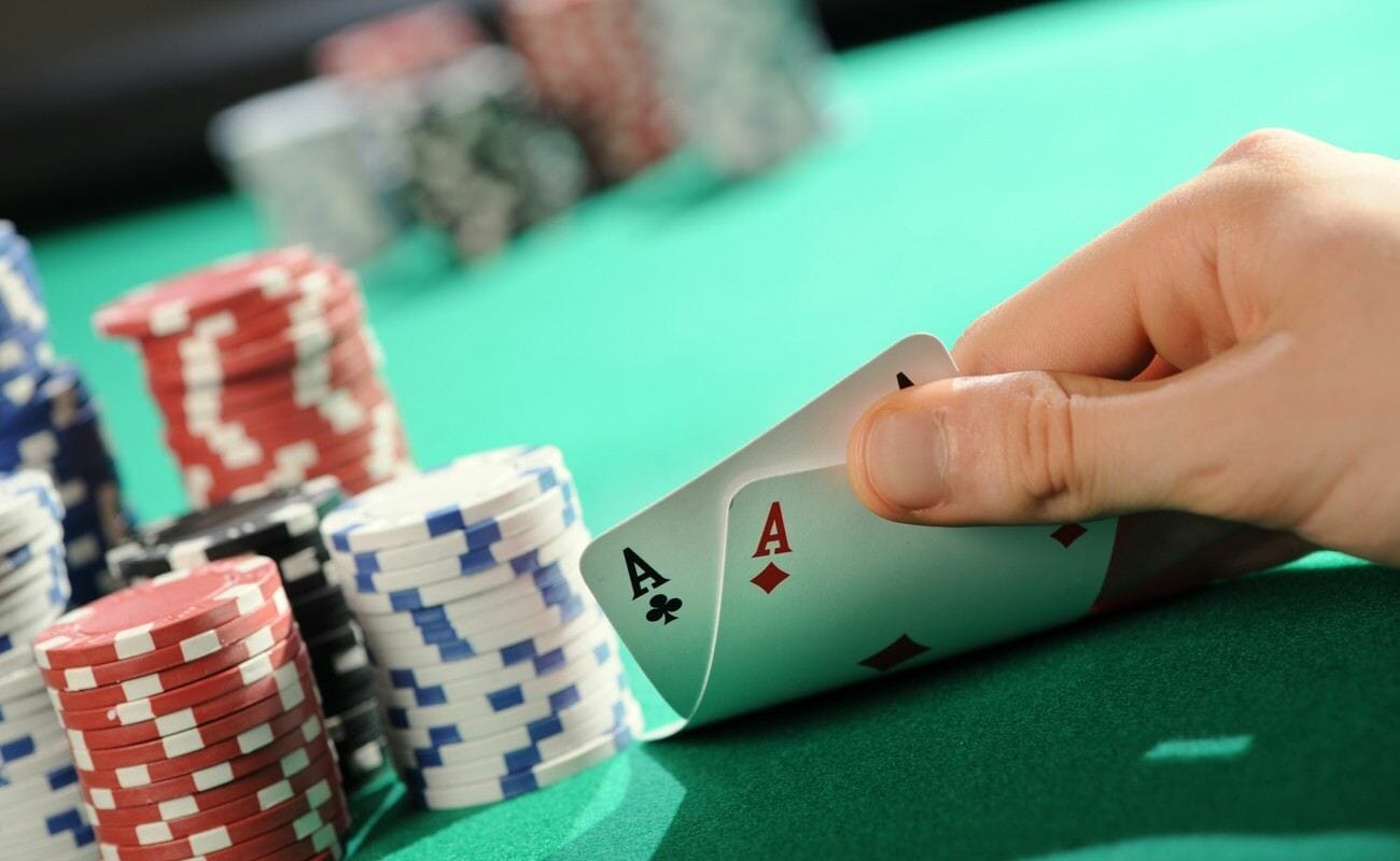 A poker player checking their hole cards next to their stacks of poker chips. They see two aces.