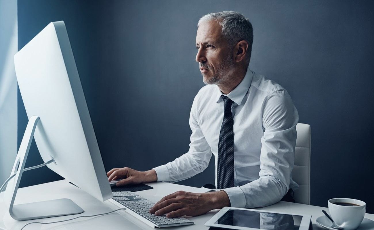 An auditor wearing a collared shirt and tie working at their computer.