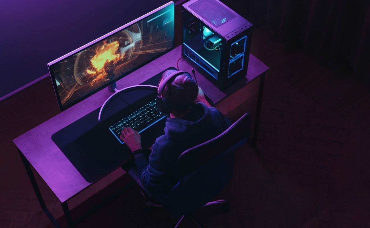 A young man playing an action game on his gaming PC. The room is bathed in lavender light.