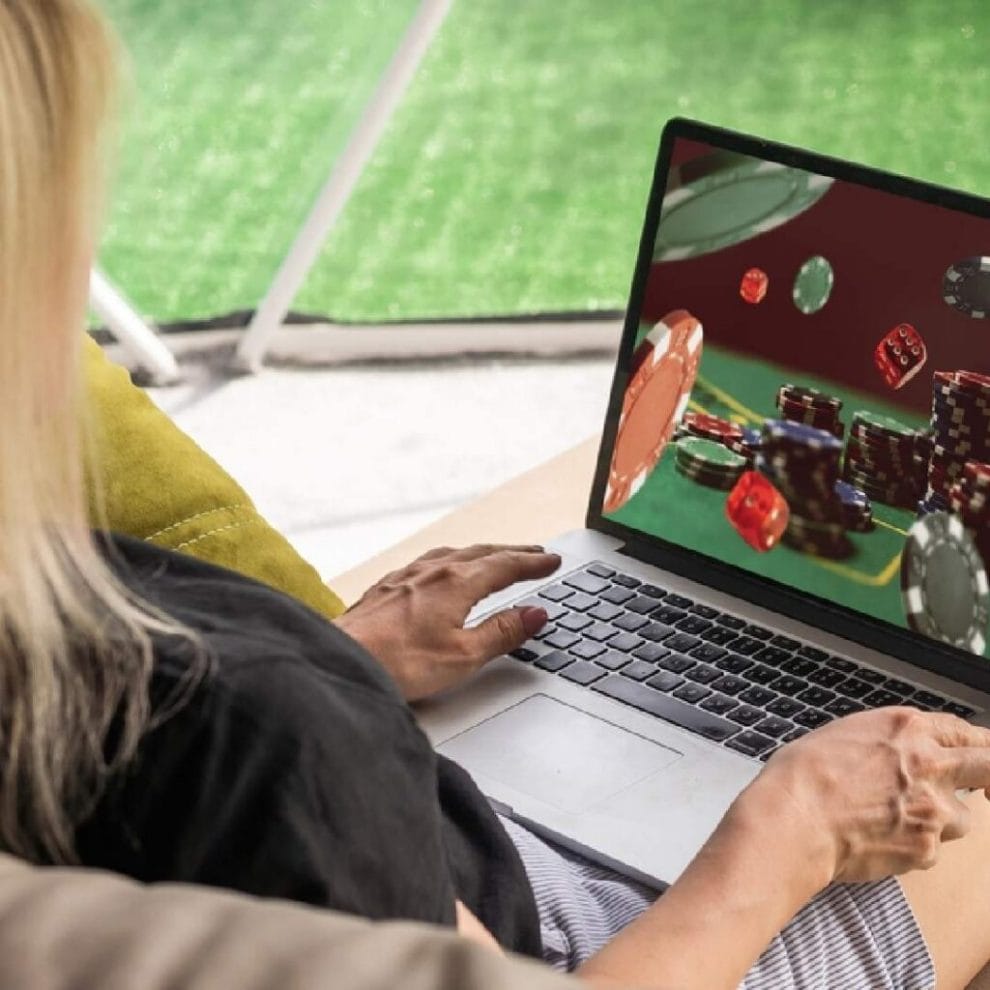 A woman on her laptop with poker chips and die playing on the screen