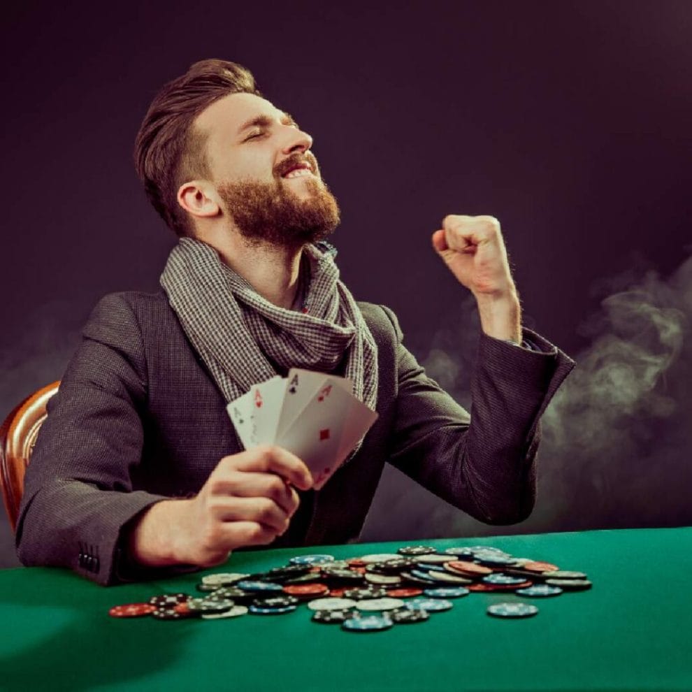A man holds up four aces in his hand and celebrates at a poker tale