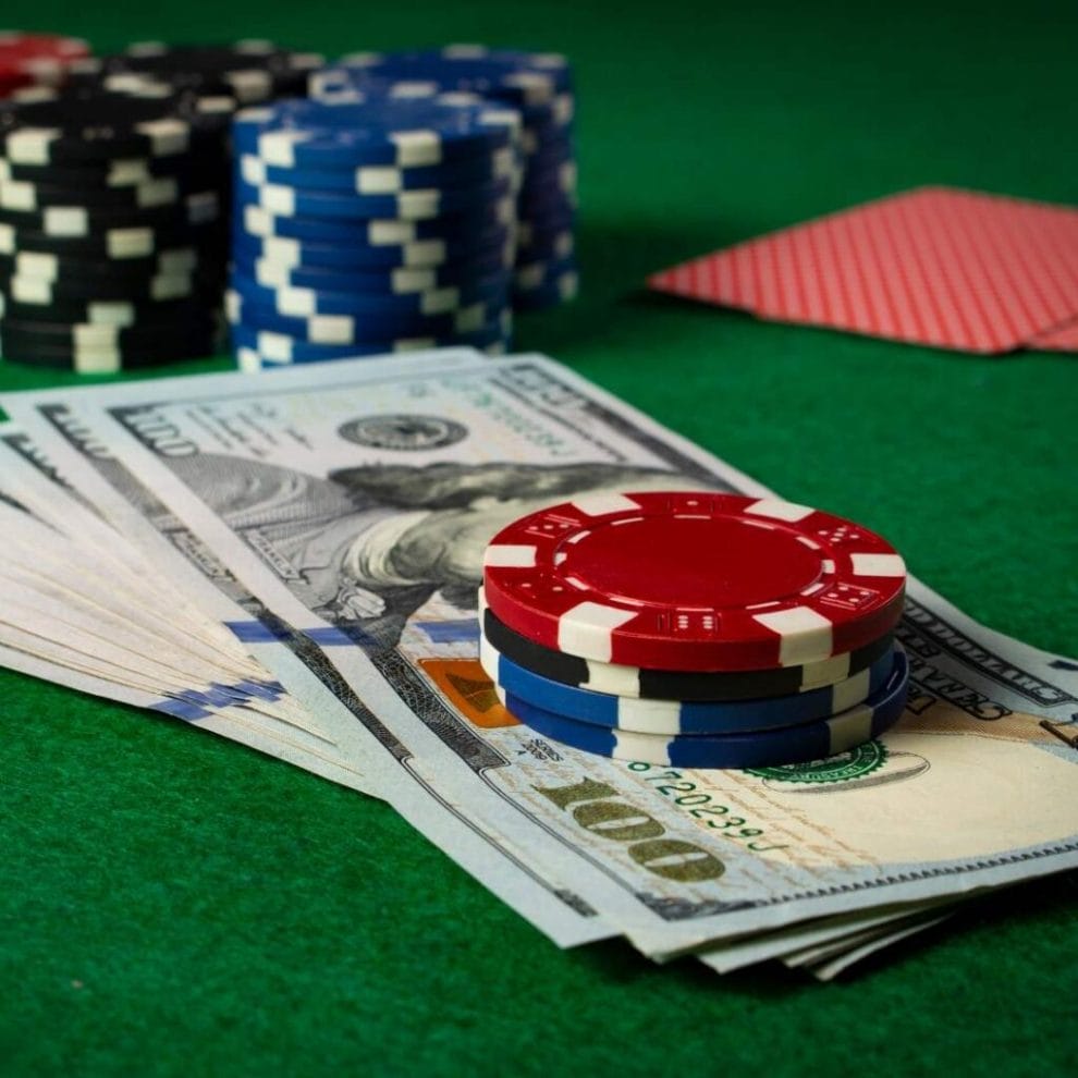 A small stack of poker chips sits on $100 bills on a poker table.