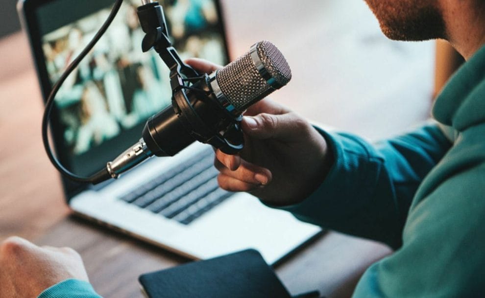 A man recording on a microphone in front of a laptop.