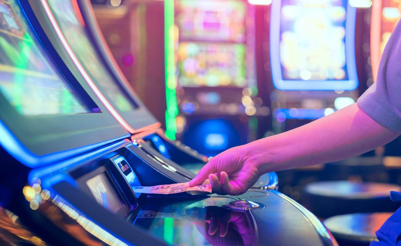 A person putting money into a slot machine at a casino.