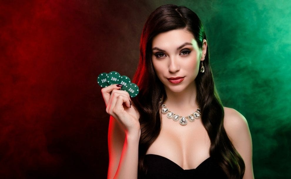 A beautiful brunette woman holds up four $100 poker chips in her right hand.