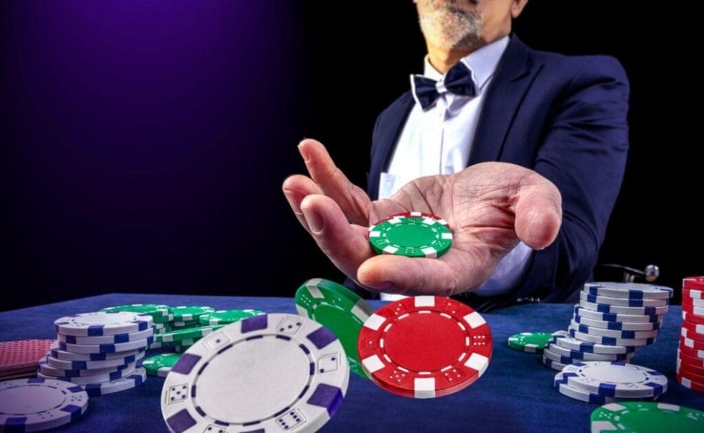 A man wearing a tuxedo holding two casino chips in his hand with arm extended out.