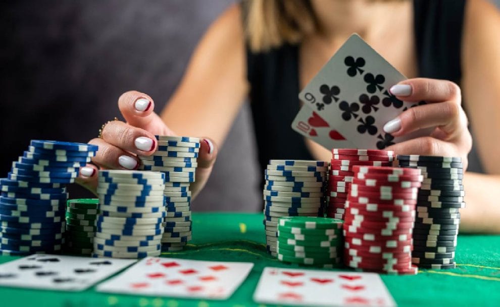 A woman poker player with a 10 and 9 in her hand picking up a chip from the stack