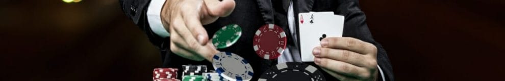 Close up of a man holding two aces and throwing chips onto a poker table
