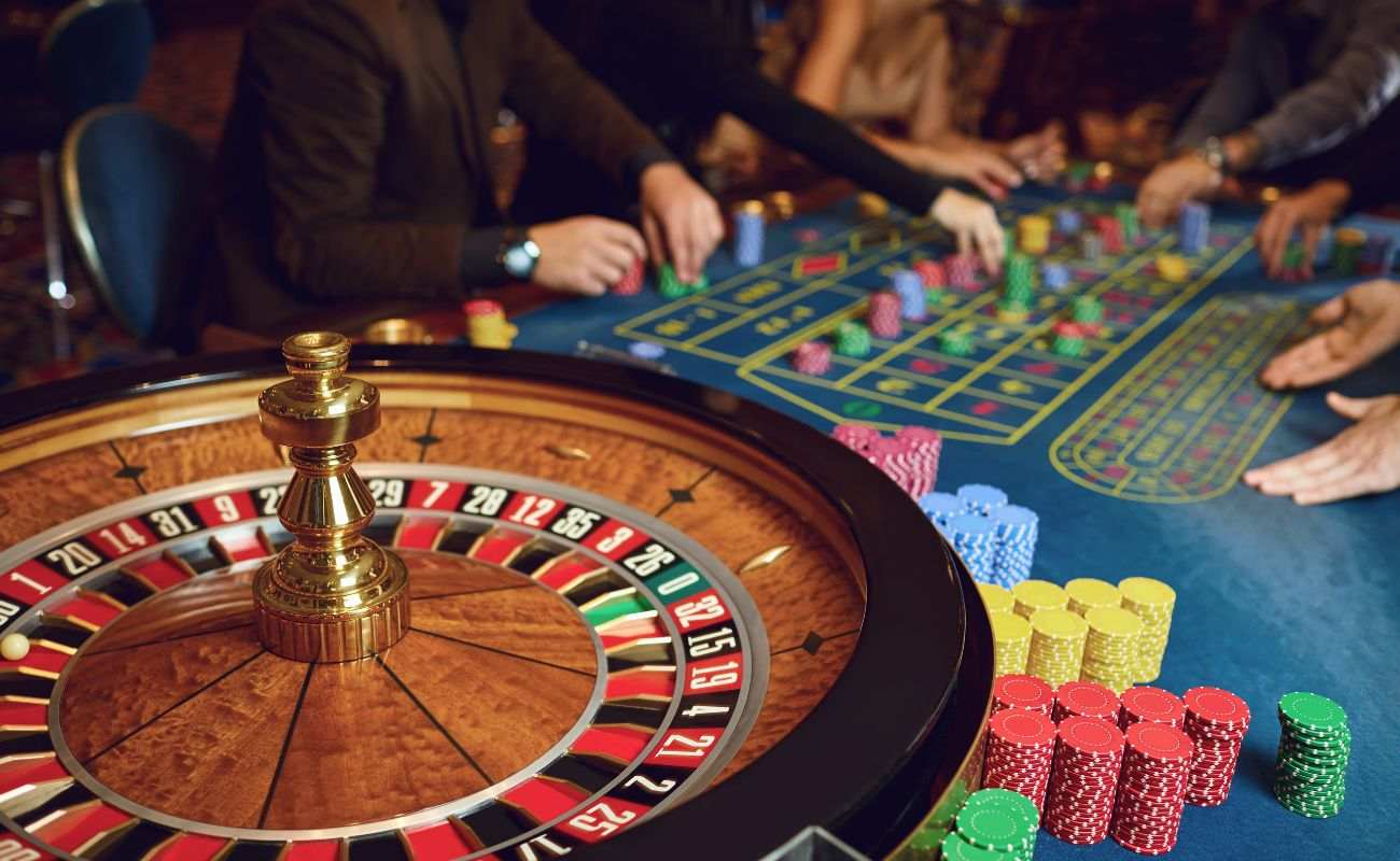 a wooden roulette wheel in focus with people betting on the roulette table in a casino in the blurred background