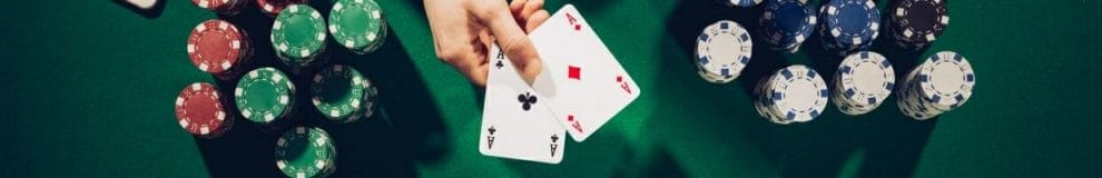 a person holding out a pair of ace playing cards above a green felt poker table with poker chips stacked on it