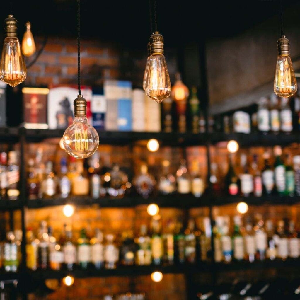 ambient light bulbs hanging from the roof of a bar with blurred alcohol bottles lined up on the shelves in the background