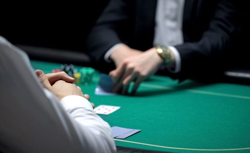 a player is sitting opposite the dealer and checking their hole cards during a poker game 