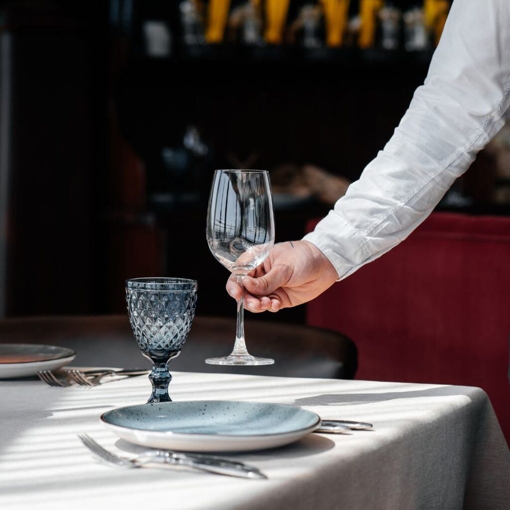 a waiter placing a wine glass down on a set table in a restaurant