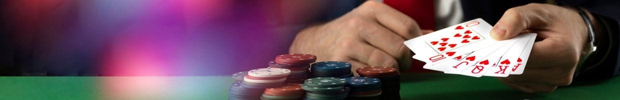 a person holding a royal flush of hearts above a green felt poker table with poker chips stacked on it in a casino 