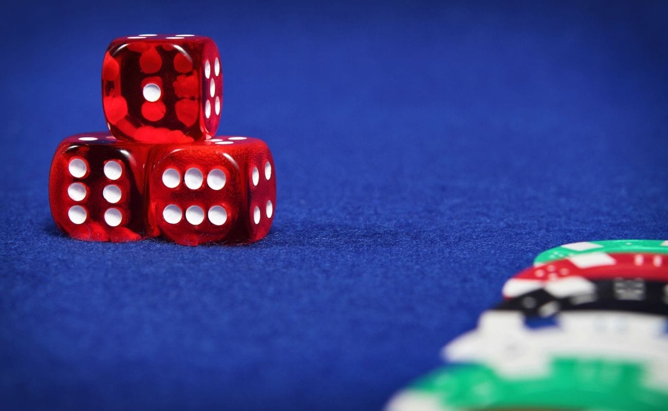 three red six-sided casino dice stacked in a pyramid on a blue felt surface with blurred casino chips in the foreground