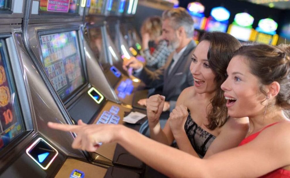 two women celebrating a win while playing on a slot machine in a casino