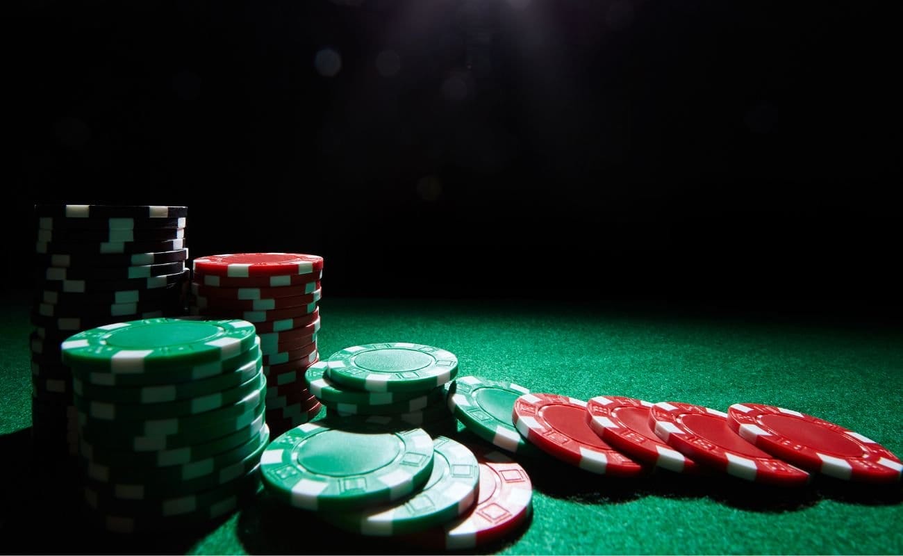 stacks of green, red and black poker chips on a green felt poker table with a dark shadow in the background