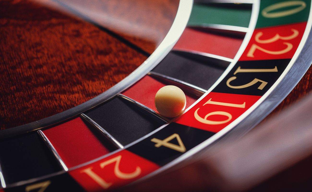 A closeup of a little white roulette ball on the red number 19 in a wooden roulette wheel.