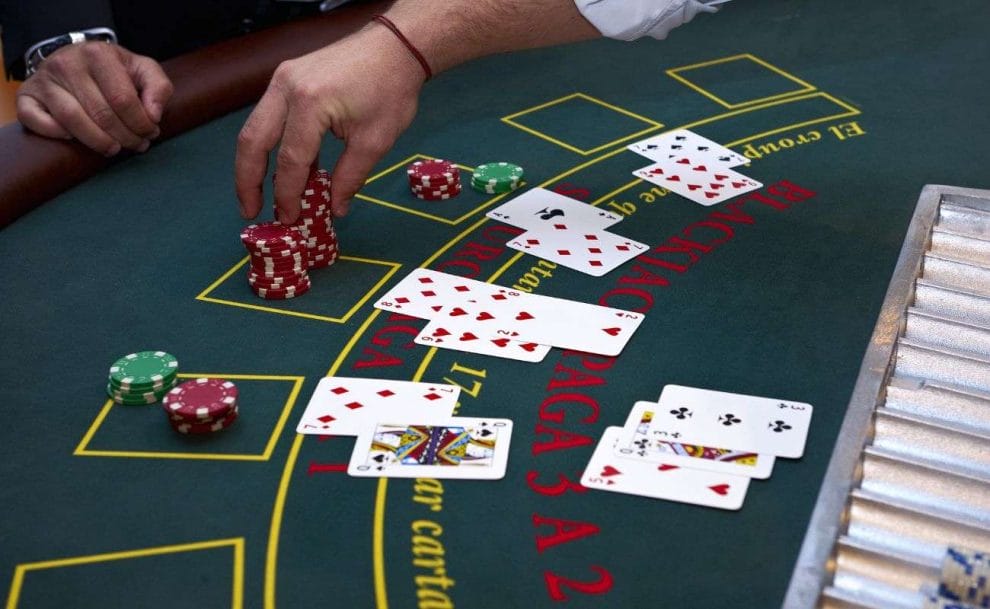 a dealer reaches over a blackjack table, with playing cards face up during a game of blackjack, to collect from a stack of red poker chips