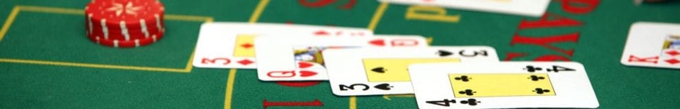 playing cards face up in front of a short stack of red poker chips on a green felt blackjack table in a casino