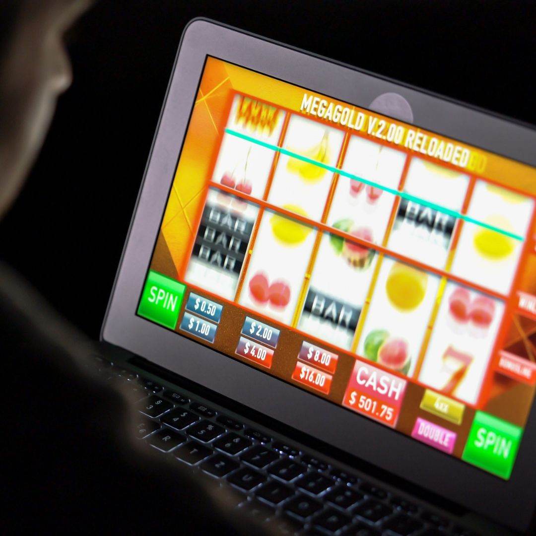 on over the shoulder view of a man playing online slots on a laptop in the dark