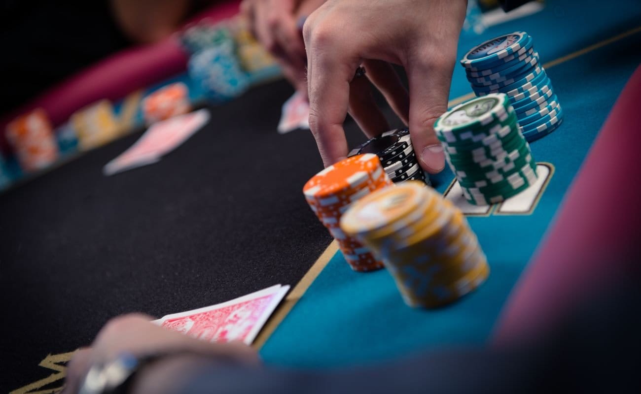 A person’s hand places a stack of black poker chips on the poker table in front of them.