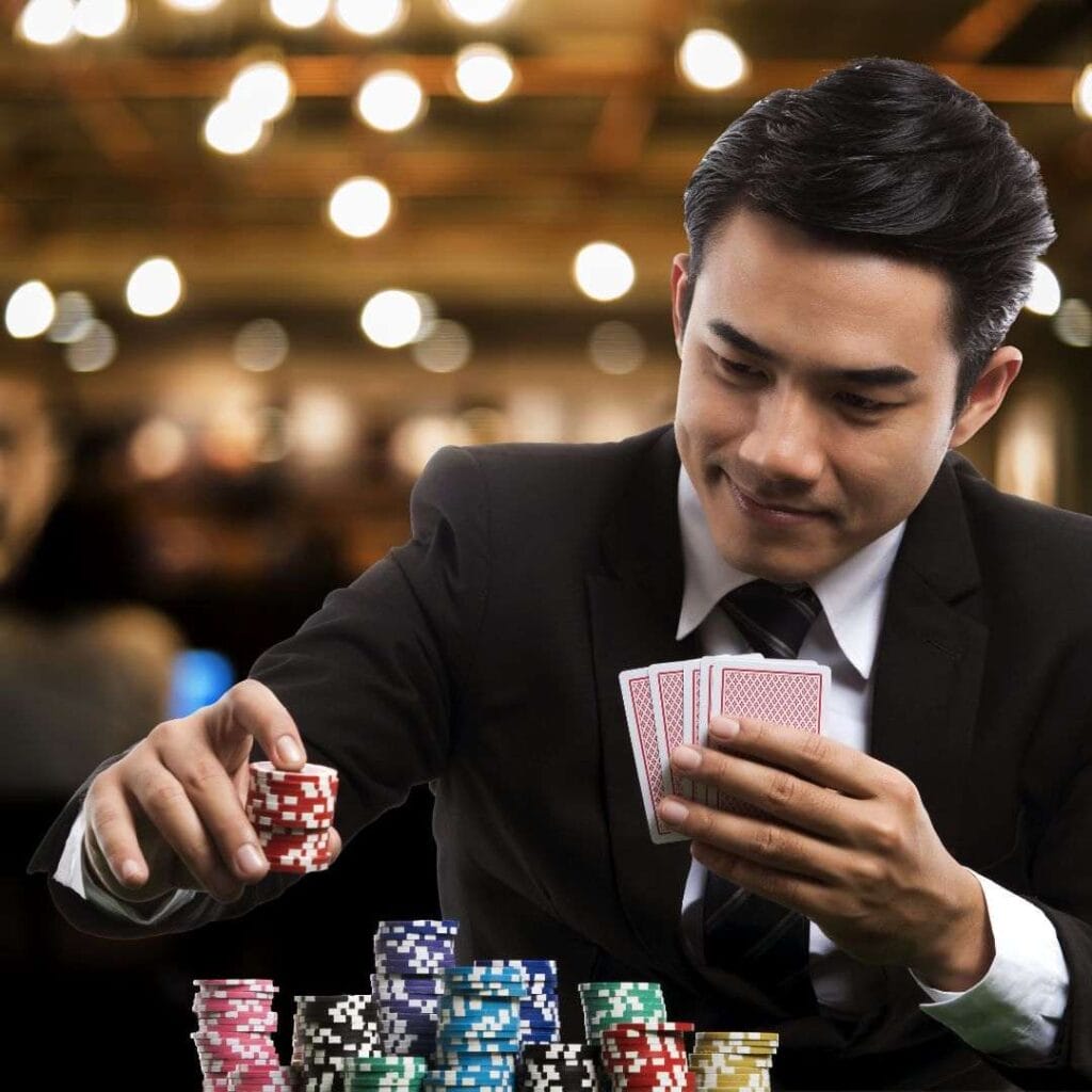 A person wearing a suit smiles while holding playing cards.