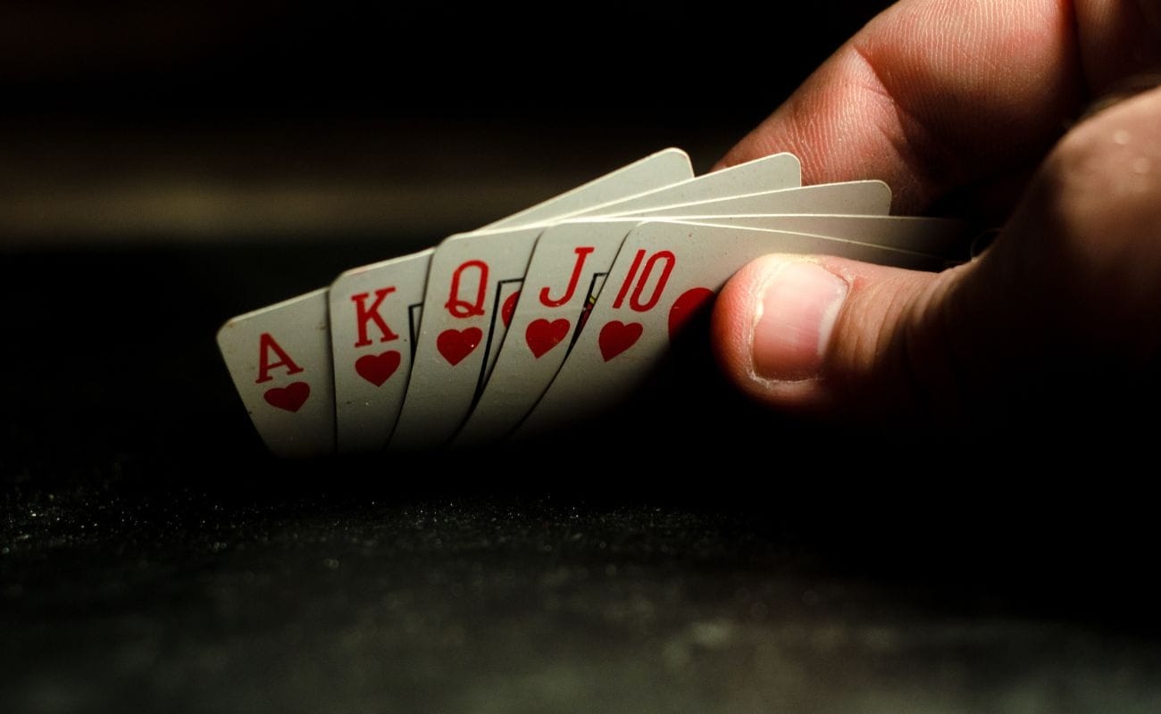 a person’s hand flipping up a royal flush of hearts on a black surface 