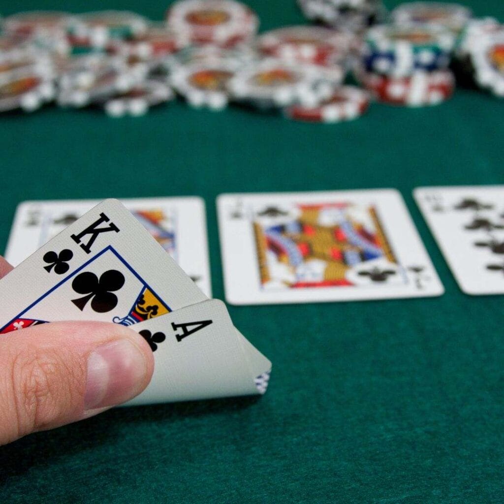 an ace and king of clubs playing cards being flipped up on a green felt poker table with a queen, jack, ten face up on the table in the blurred background and blurred poker chips further back