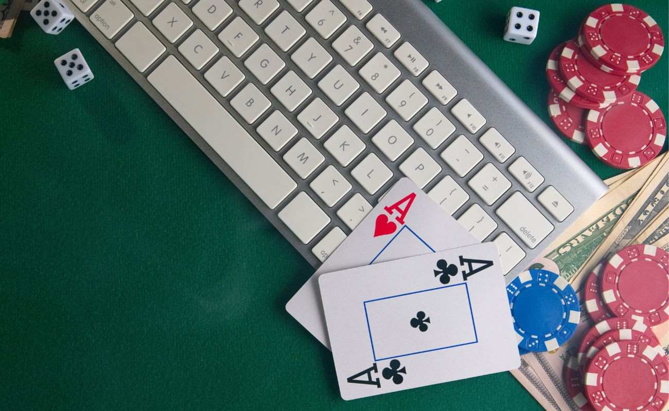 a pair of ace playing cards, poker chips, dice, money and a computer keyboard on a green felt poker table 